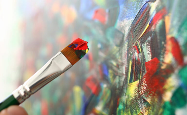 Hand holds brush with watercolors and paints picture